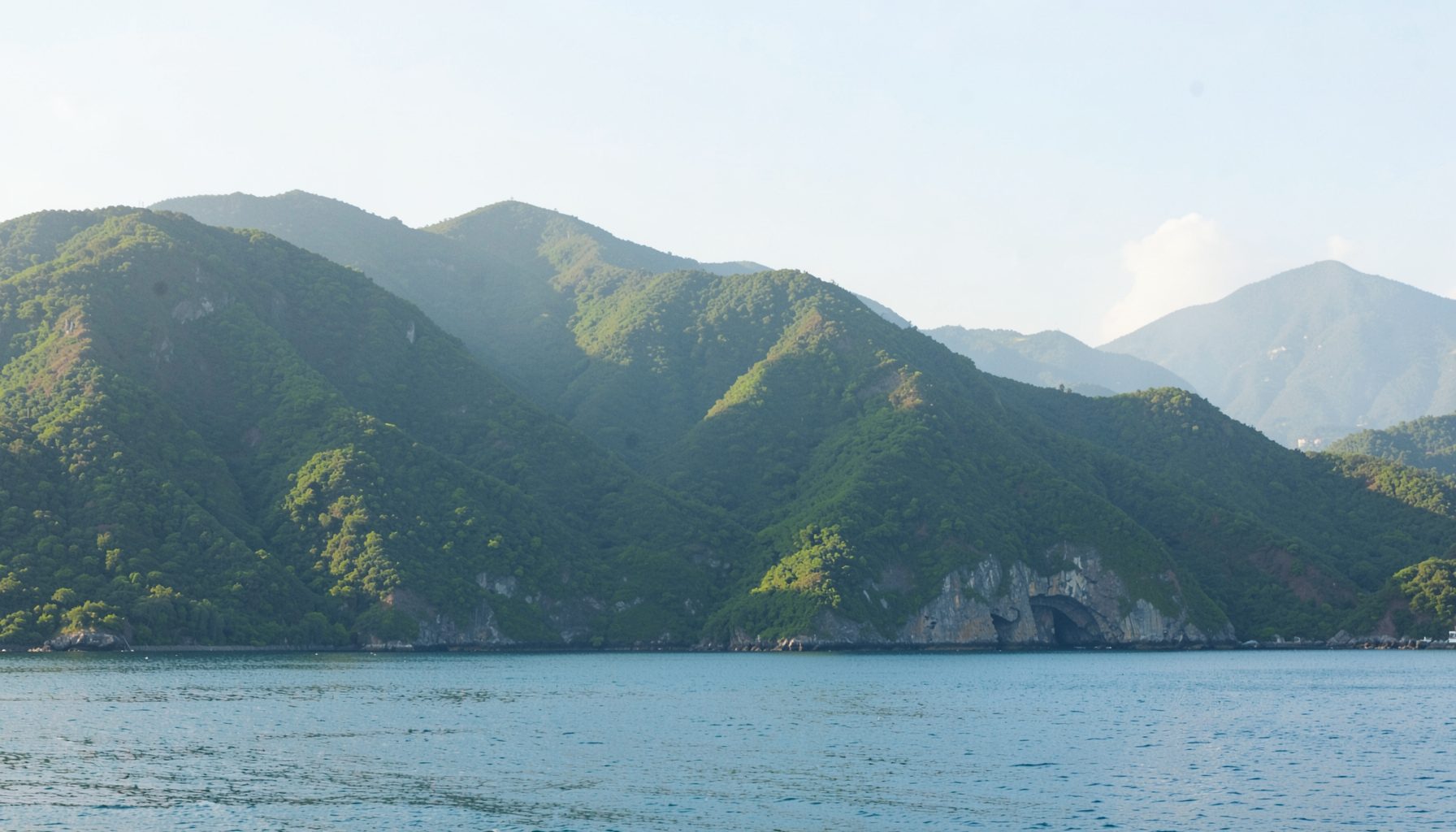 A green mountain range meeting a calm sea under soft daylight, peaceful coastal mood