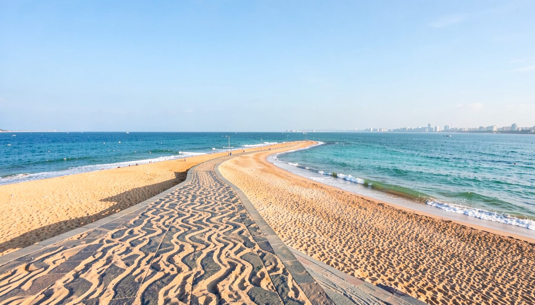 A panoramic view of Copacabana beach with its distinctive wave-patterned promenade curving along golden sand, turquoise water, and hills rising in the distance