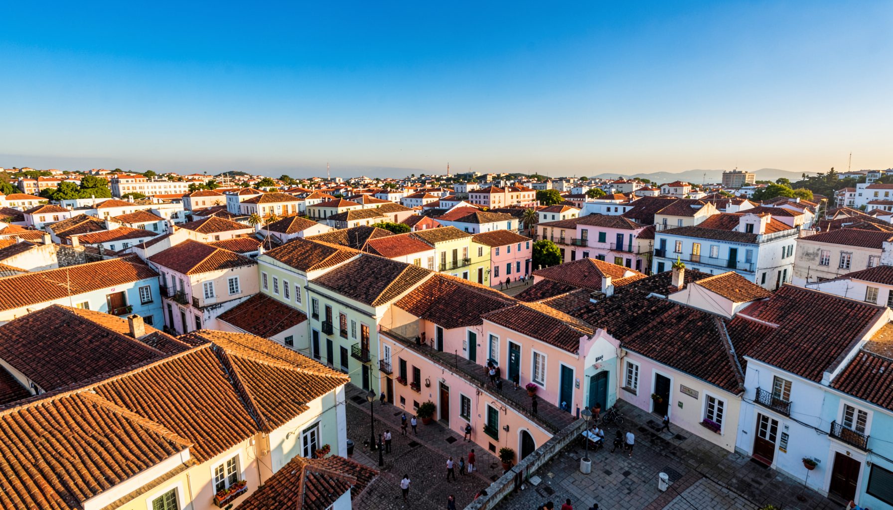 A sweeping aerial view of Salvador's historic Pelourinho district with pastel-colored colonial buildings and terracotta rooftops under a bright blue sky