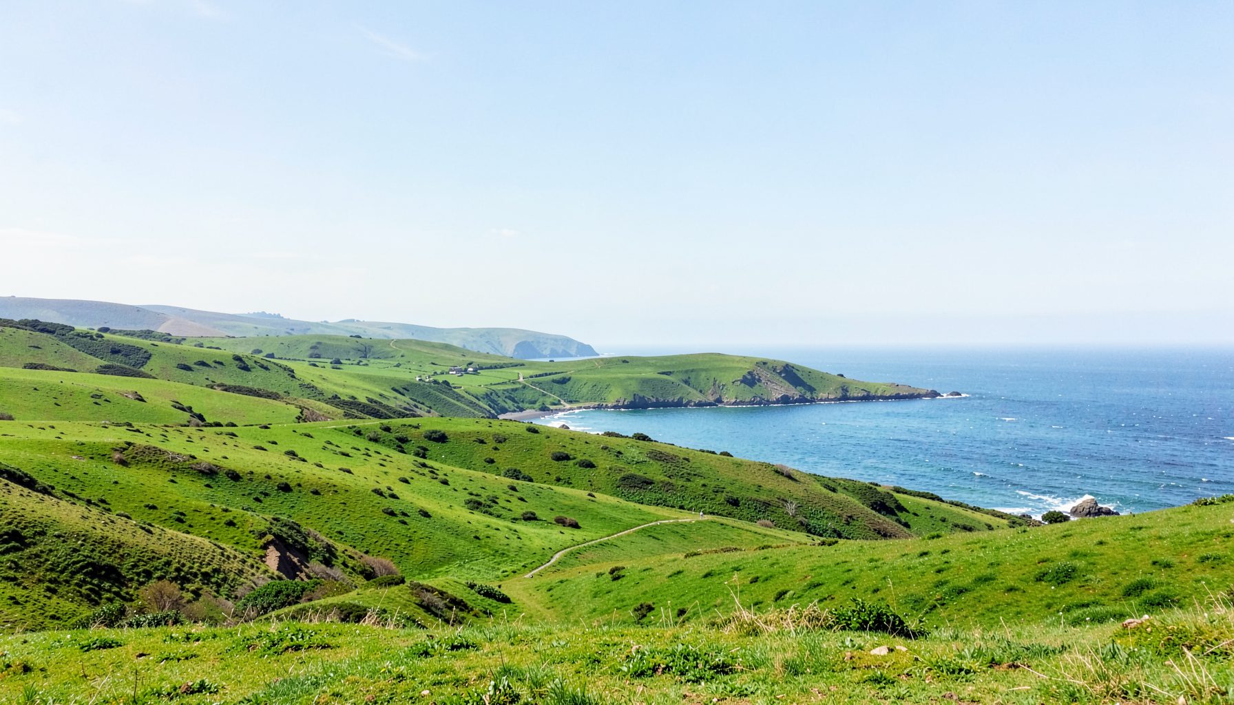 A wide green landscape of rolling hills and coastline under a bright sky, calm and inviting in tone
