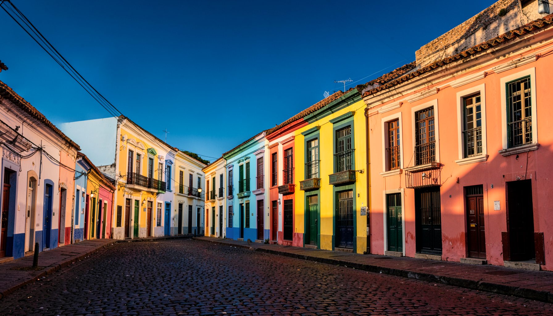 Colorful colonial buildings lining a cobblestone street in Salvador, Bahia, with warm golden light and deep blue sky